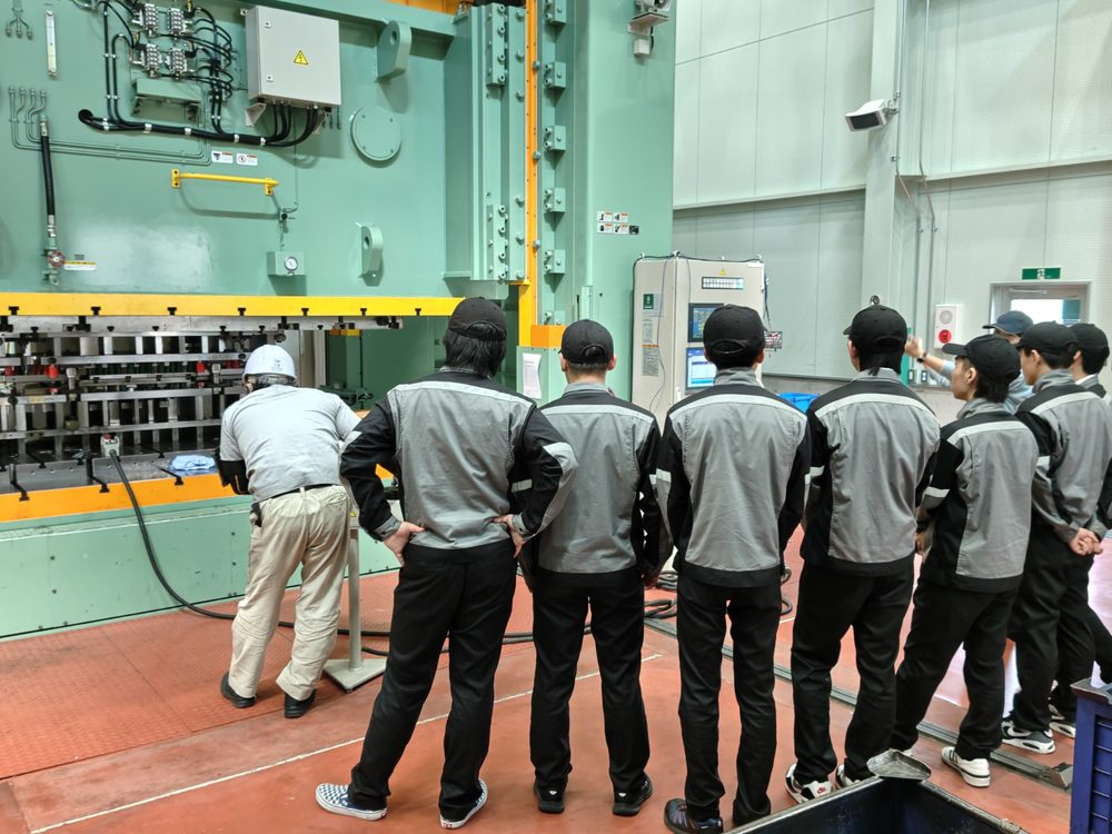 プレス機の前で説明を受ける工場見学の一団