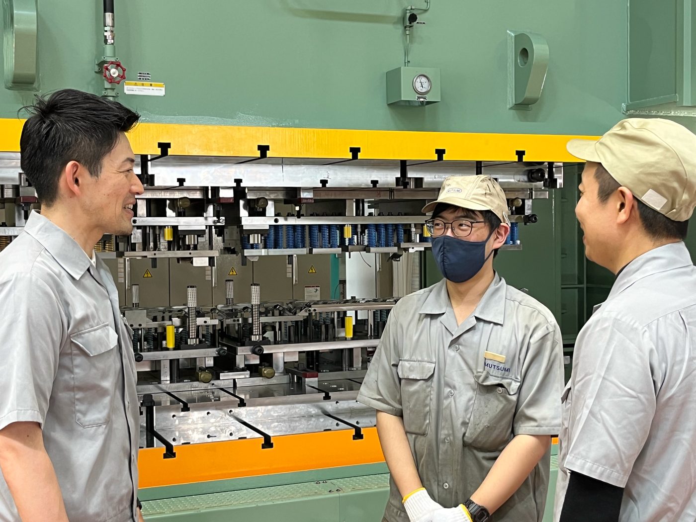 プレス機の前で相談する社員たち